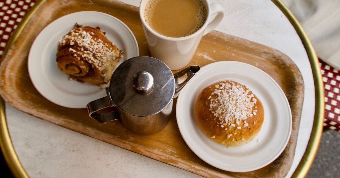Kaffekopp, kanna och två pärlsockrade bullar på ett fikabord