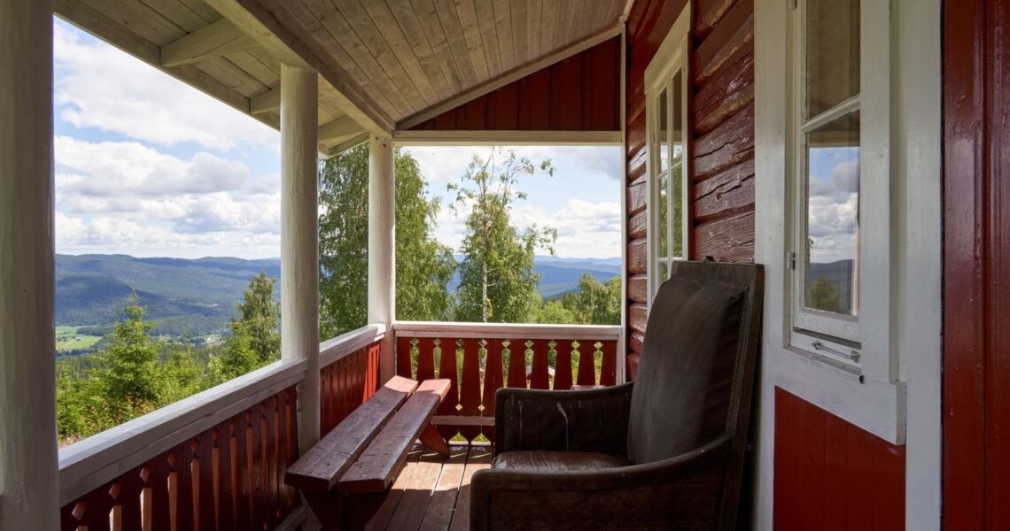Öppen veranda i rött trä med utsikt över skogsklädda berg